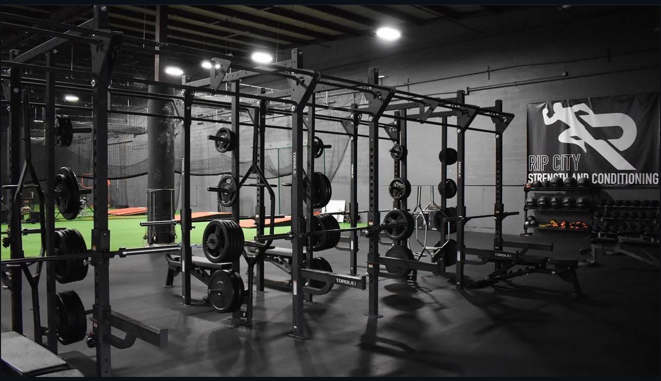 Row of loaded squat racks and benches beside the turf lane under the Rip City Strength and Conditioning banner